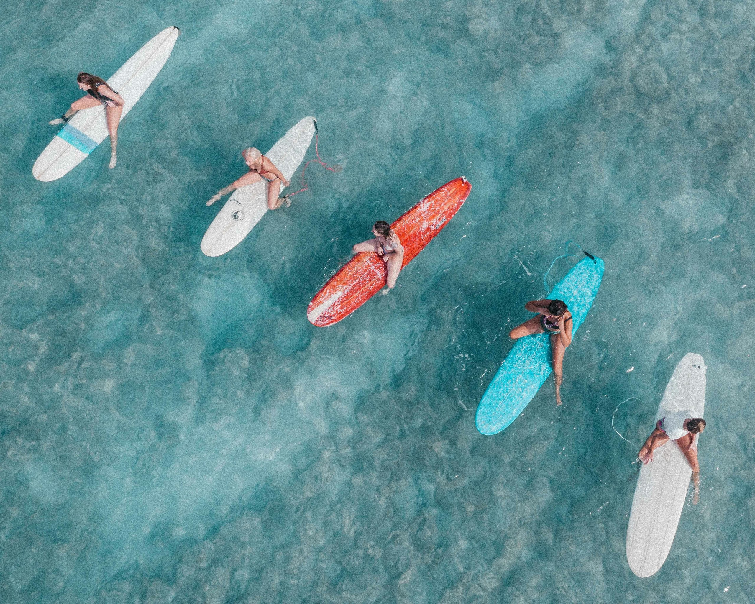 Aerial view of people resting on colorful surfboards floating in turquoise ocean, seen from above.